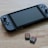 A portable gaming console is placed on a wooden surface, accompanied by two small game cartridges. The console features a screen in the center with controllers on either side, while the cartridges have colorful labels depicting game titles.