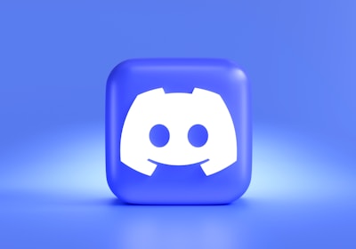 A three-dimensional blue cube featuring a white, stylized gaming controller symbol associated with a popular communication platform, set against a gradient blue background.